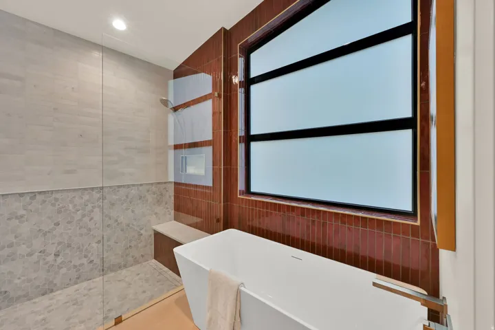 Contemporary bathroom featuring a freestanding tub with wall-mounted fixture, a frosted window with dark trim, and a shower enclosure with a built-in bench