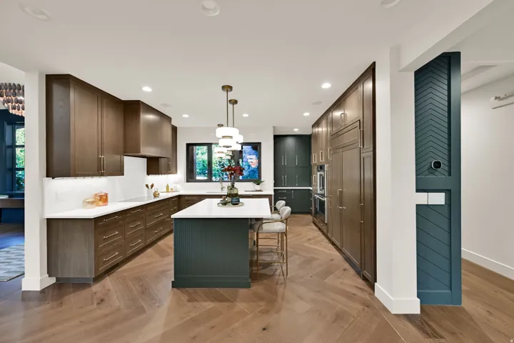 Kitchen featuring herringbone wood-finish flooring, a central island with a white countertop, dark wood-finish cabinetry, built-in stainless steel appliances, and recessed lighting