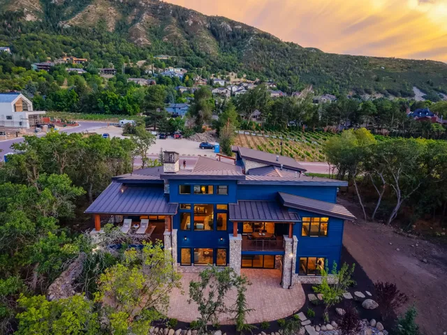 Contemporary residence featuring a blue exterior, multiple rooflines, a brick patio, and expansive windows