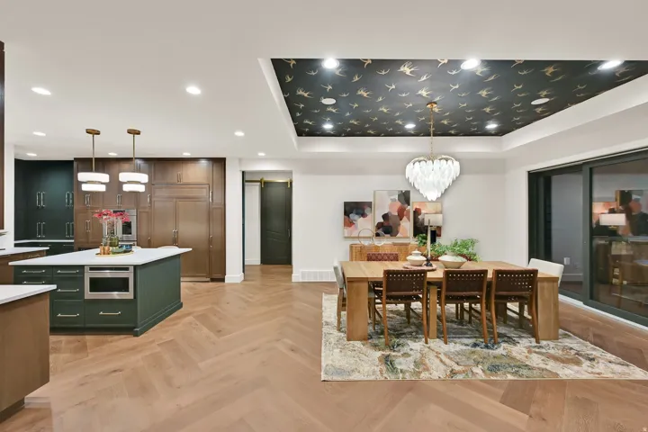 Open-concept living space featuring wood-finish flooring in a herringbone pattern, a kitchen island with integrated microwave, built-in cabinetry, recessed lighting, and a tray ceiling with decorative wallpaper and a central chandelier