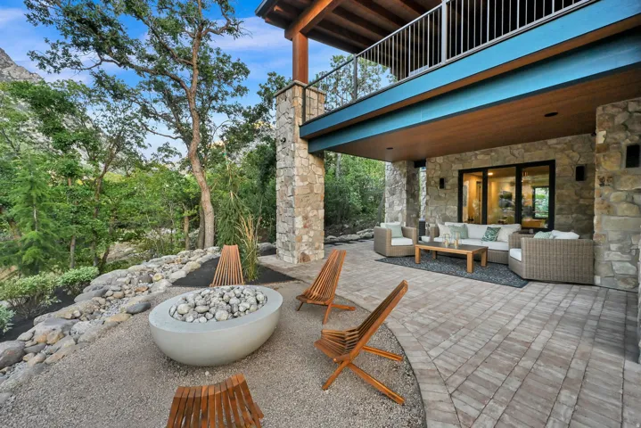 Expansive outdoor living area featuring a stone-clad exterior, covered patio with recessed lighting, and a contemporary fire pit