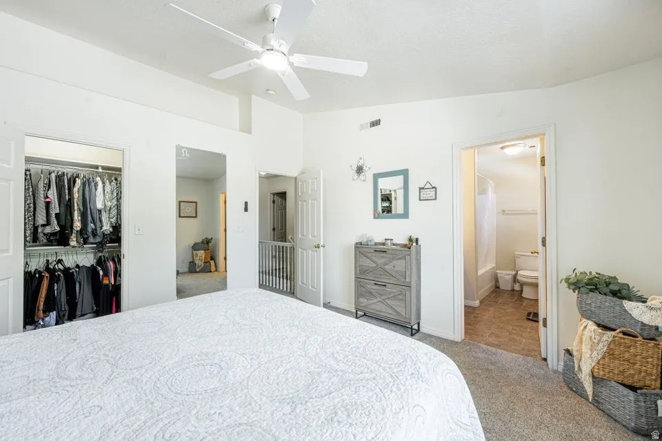Bedroom featuring a white ceiling fan, high ceilings, carpet flooring, a walk-in closet, and an en-suite bathroom with a tub and toilet