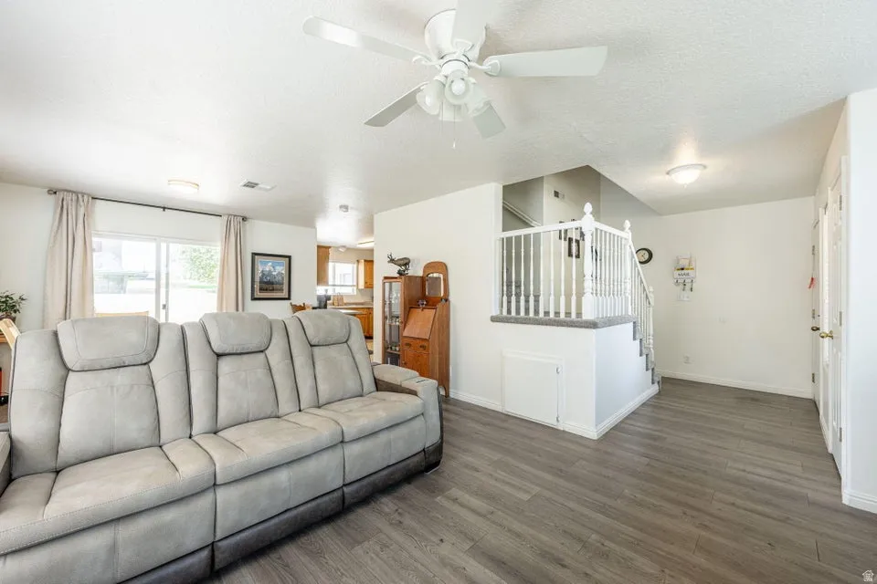 Spacious living area featuring wood-finish flooring, a white ceiling fan, and a staircase with white balusters