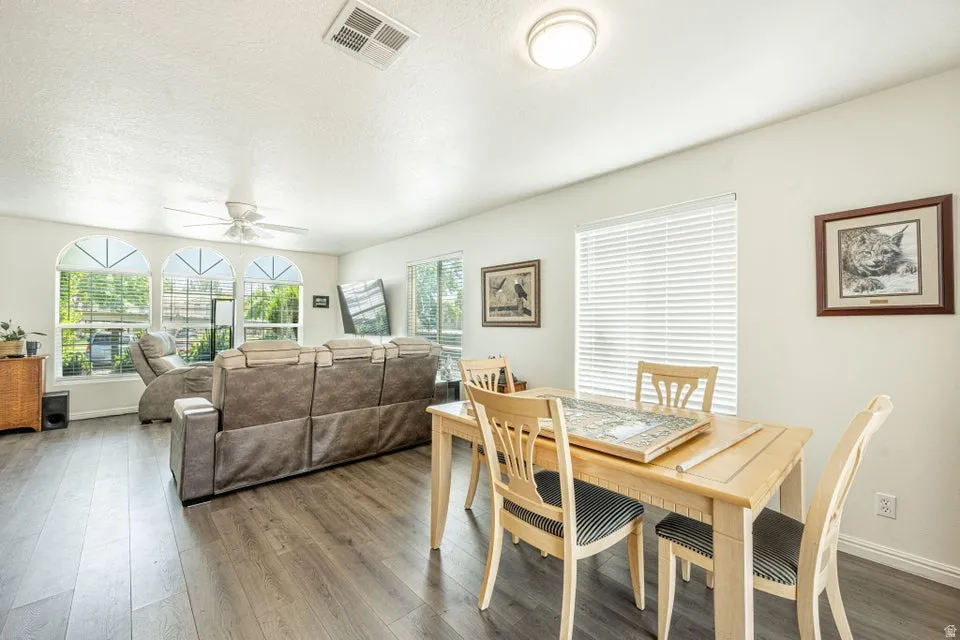 Open-concept living area featuring wood-finish flooring, a ceiling fan, and multiple arched windows
