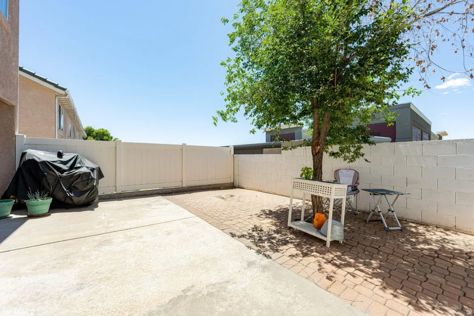 Private outdoor patio featuring a combination of concrete and paver flooring, mature tree, white block wall, and white vinyl fencing