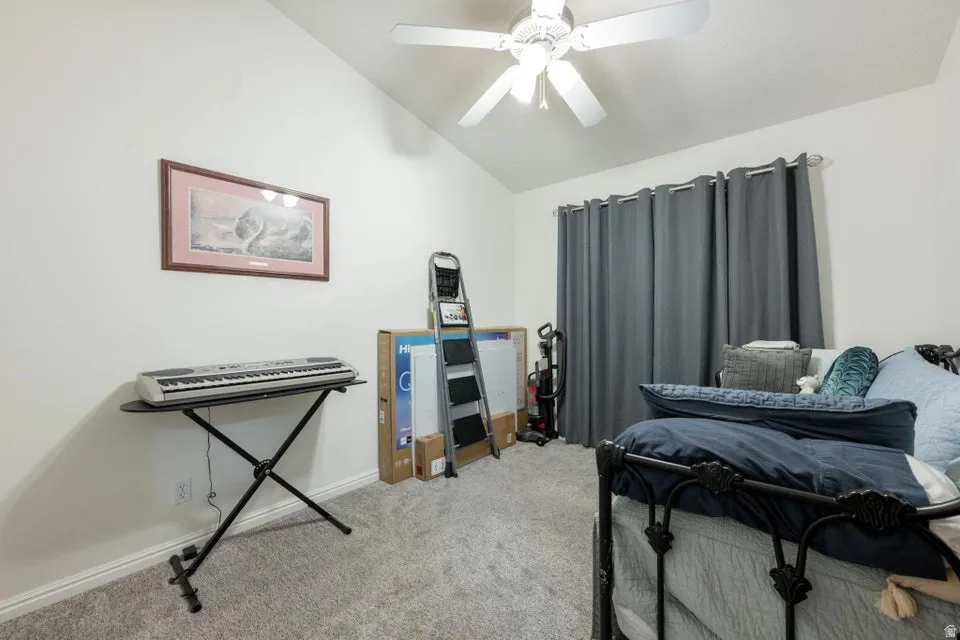 Room featuring vaulted ceilings, a ceiling fan, light gray carpeting, and a window with dark gray drapery