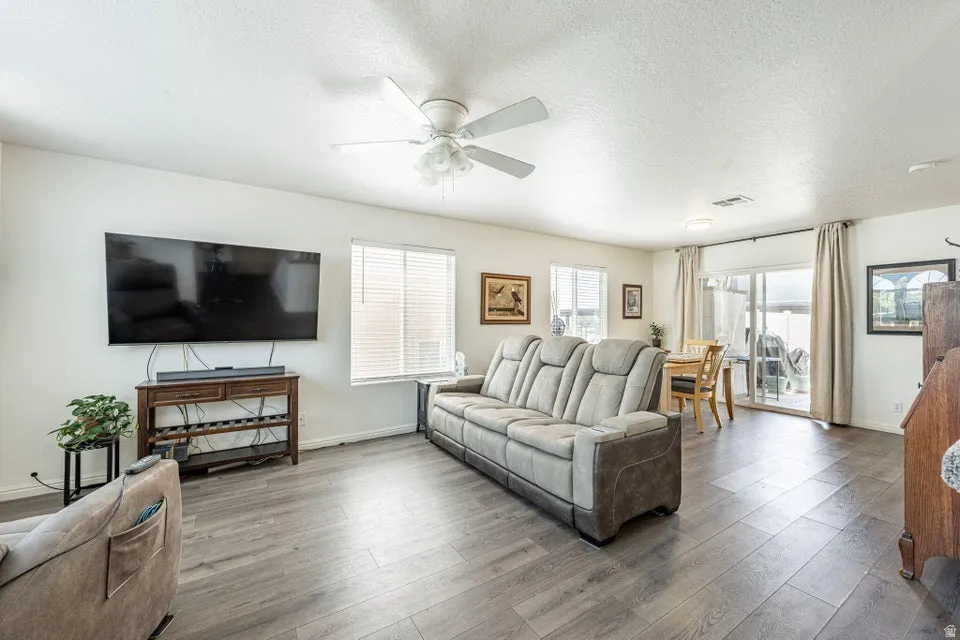 Spacious living area featuring wood-finish flooring, white walls, and a ceiling fan