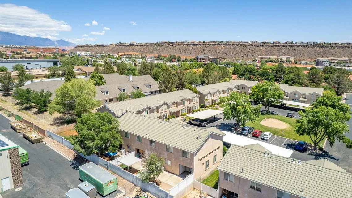 Townhome community featuring multi-story residences with light-colored roofs, ample parking areas including covered spaces, mature landscaping, and distant mountain backdrops