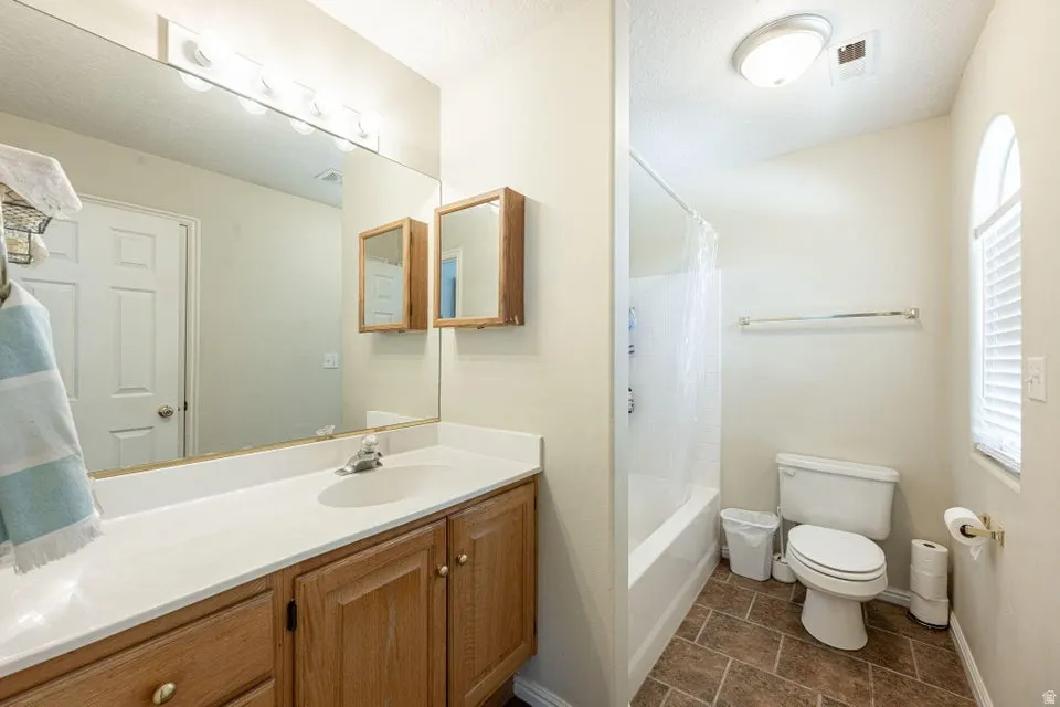Bathroom featuring a vanity with wood-finish cabinetry, a large wall-mounted mirror, and a white countertop with integrated sink