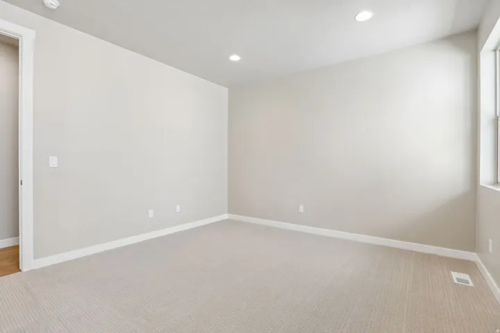Spacious room featuring neutral carpeting, light neutral wall paint, recessed lighting, and a window providing natural light