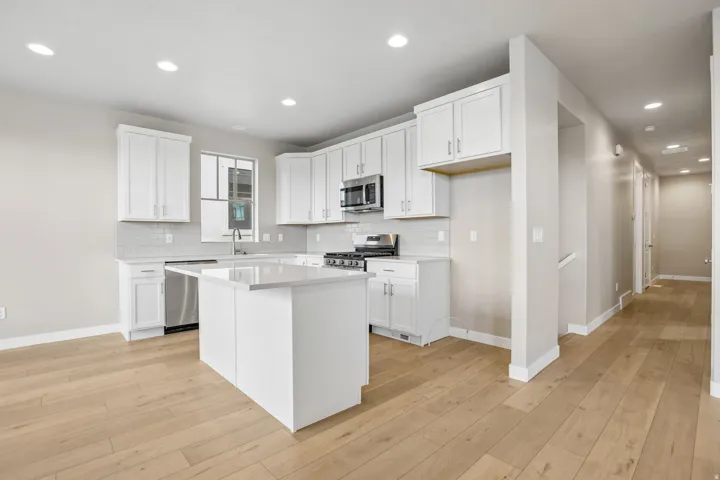 Modern kitchen featuring white shaker cabinetry, stainless steel appliances, a white subway tile backsplash, and light wood-finish flooring