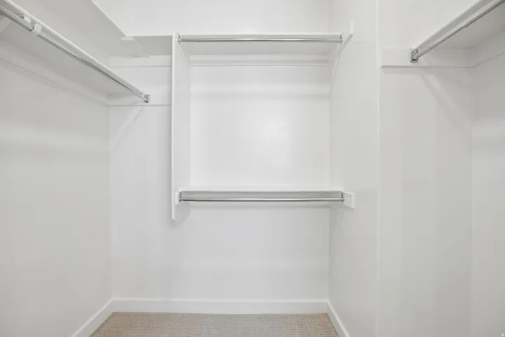 Walk-in closet featuring white shelving and chrome hanging rods