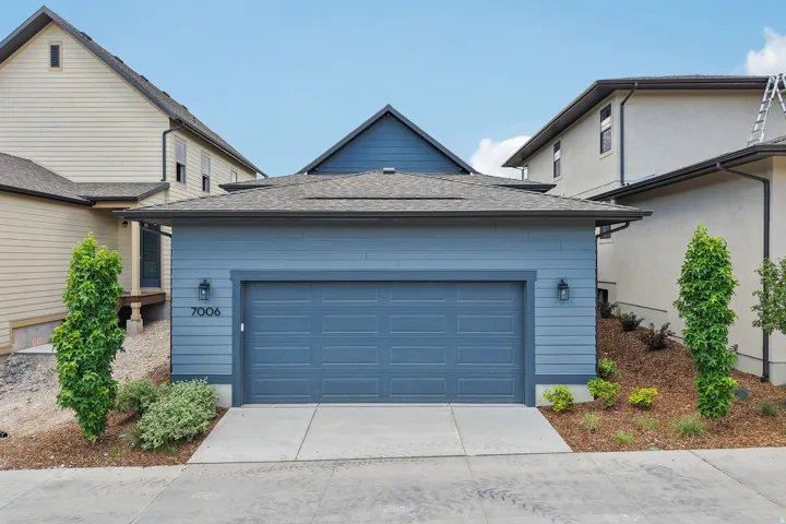 Contemporary single-car garage featuring a paneled door, blue horizontal siding, and dark sconce lighting