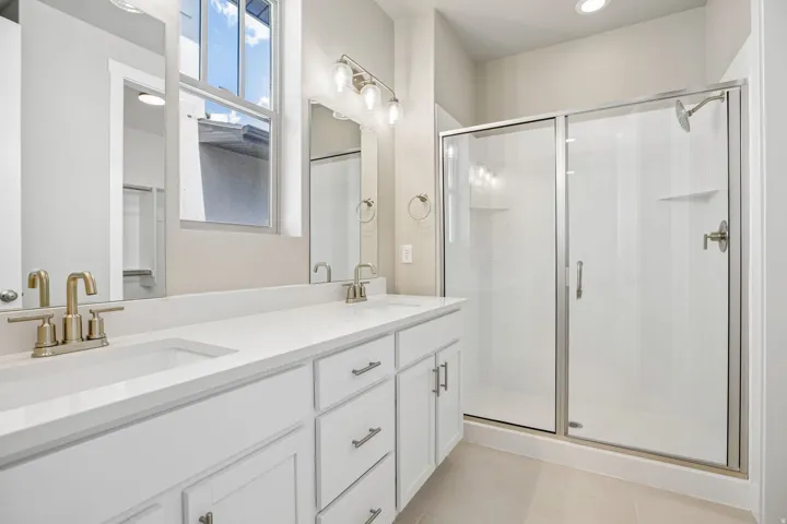 Bathroom featuring a dual vanity with white cabinetry, integrated sinks, and brushed brass fixtures
