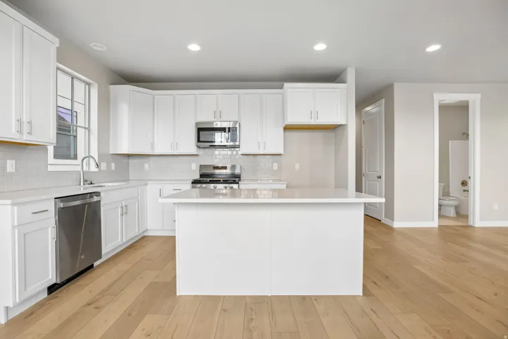 Modern kitchen featuring white shaker cabinetry, stainless steel appliances, light-toned wood-finish flooring, a central island, and recessed lighting