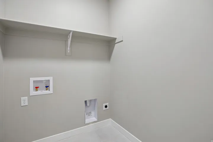Dedicated utility space featuring a wall-mounted shelf, electrical outlets, and plumbing hookups