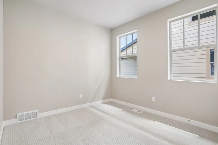 Neutral-toned room with two windows, light-colored carpet, and white baseboards