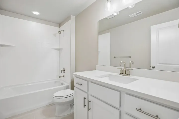 Bathroom featuring a white vanity with an integrated sink, brushed nickel fixtures, a large mirror, and a full-size bathtub with an overhead shower and built-in shelving