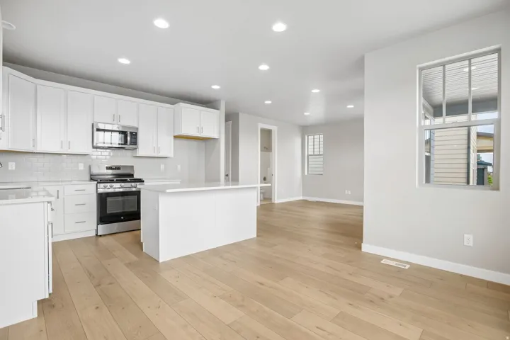 Open-concept kitchen featuring white cabinetry, stainless steel appliances, a subway tile backsplash, and light wood-finish flooring