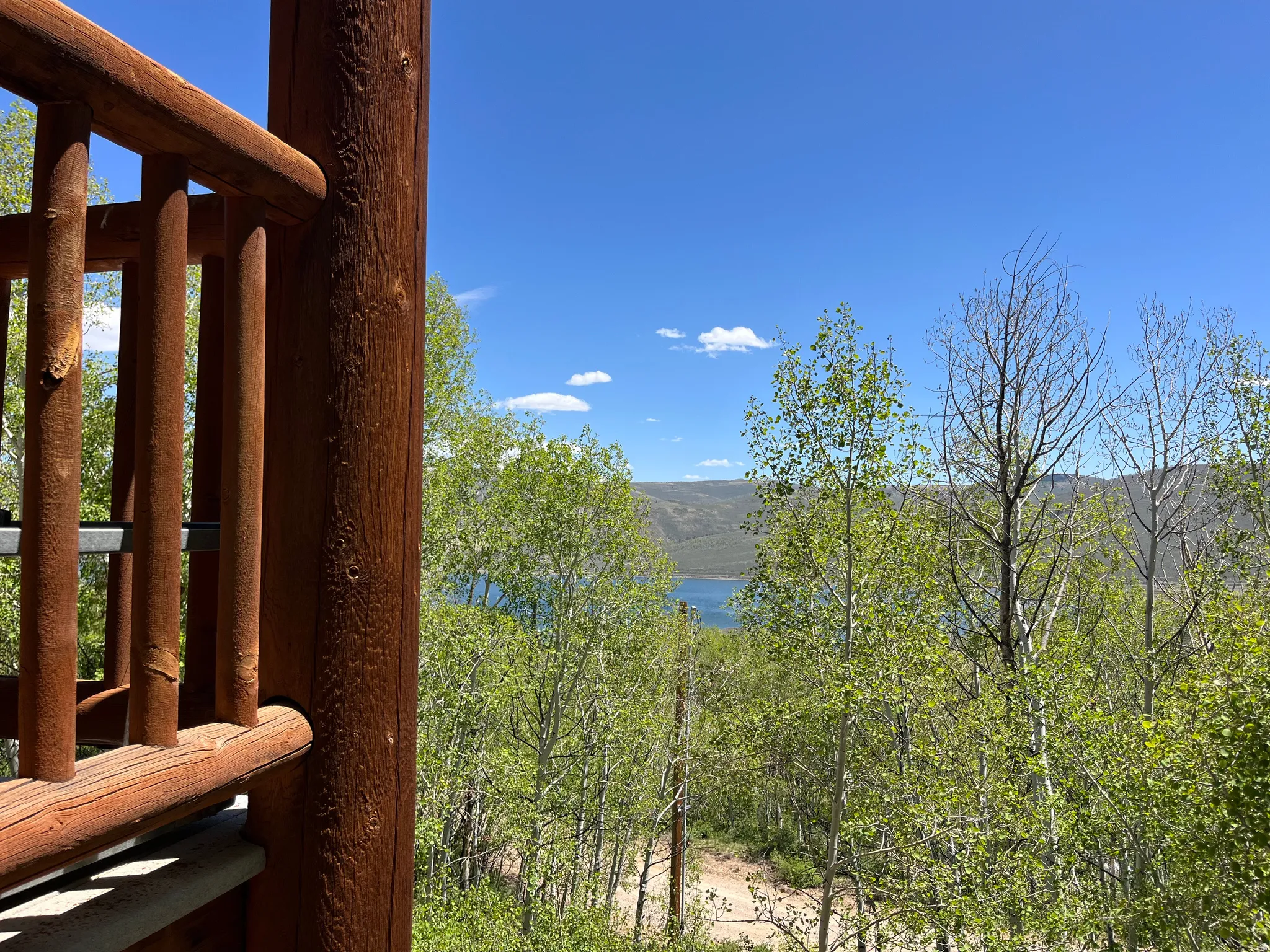 Wooden deck railing overlooking a treed landscape with water and mountains in the distance under a clear sky