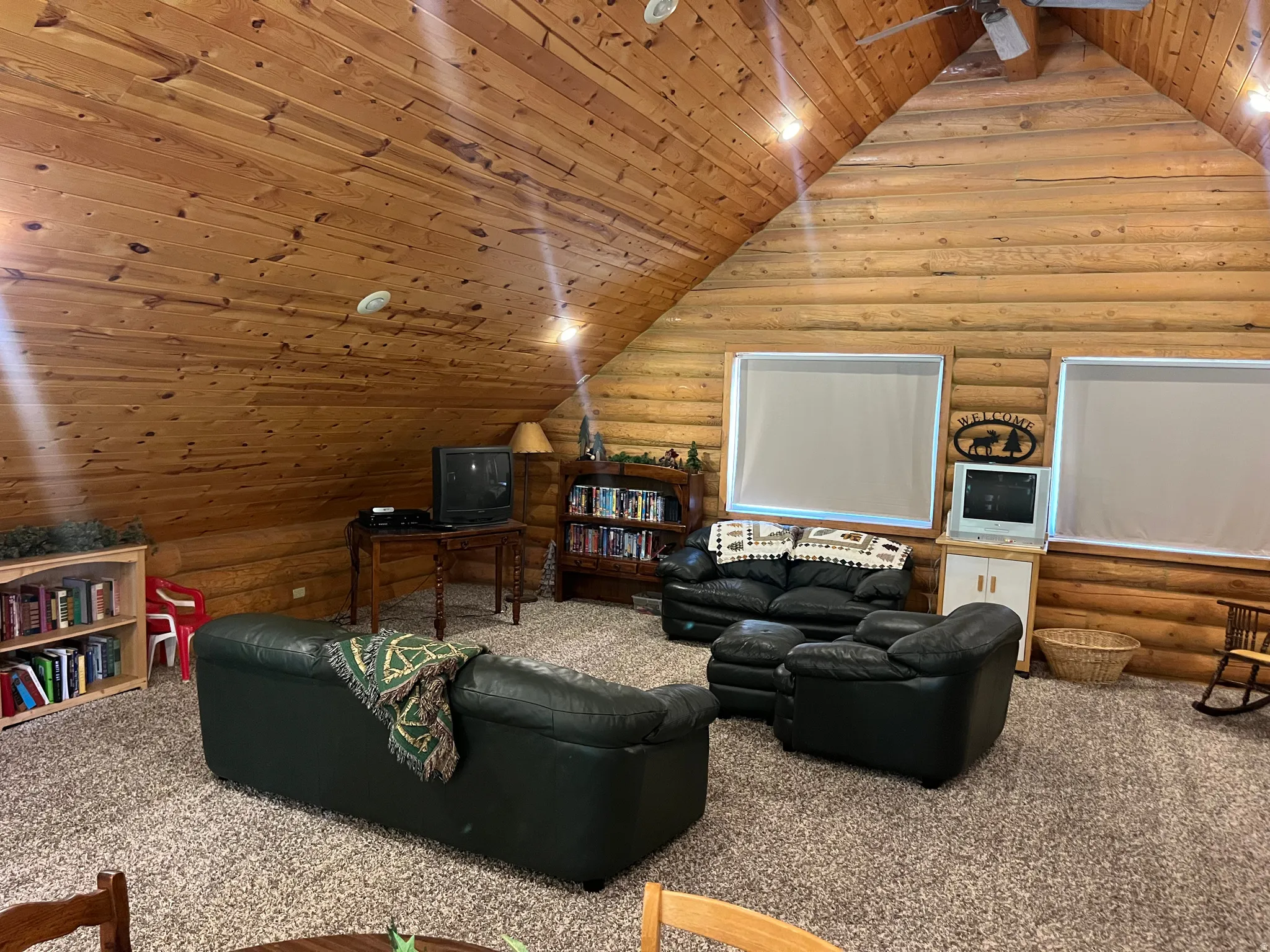 Vaulted wood-paneled ceiling with a ceiling fan, log wall construction, and two recessed windows