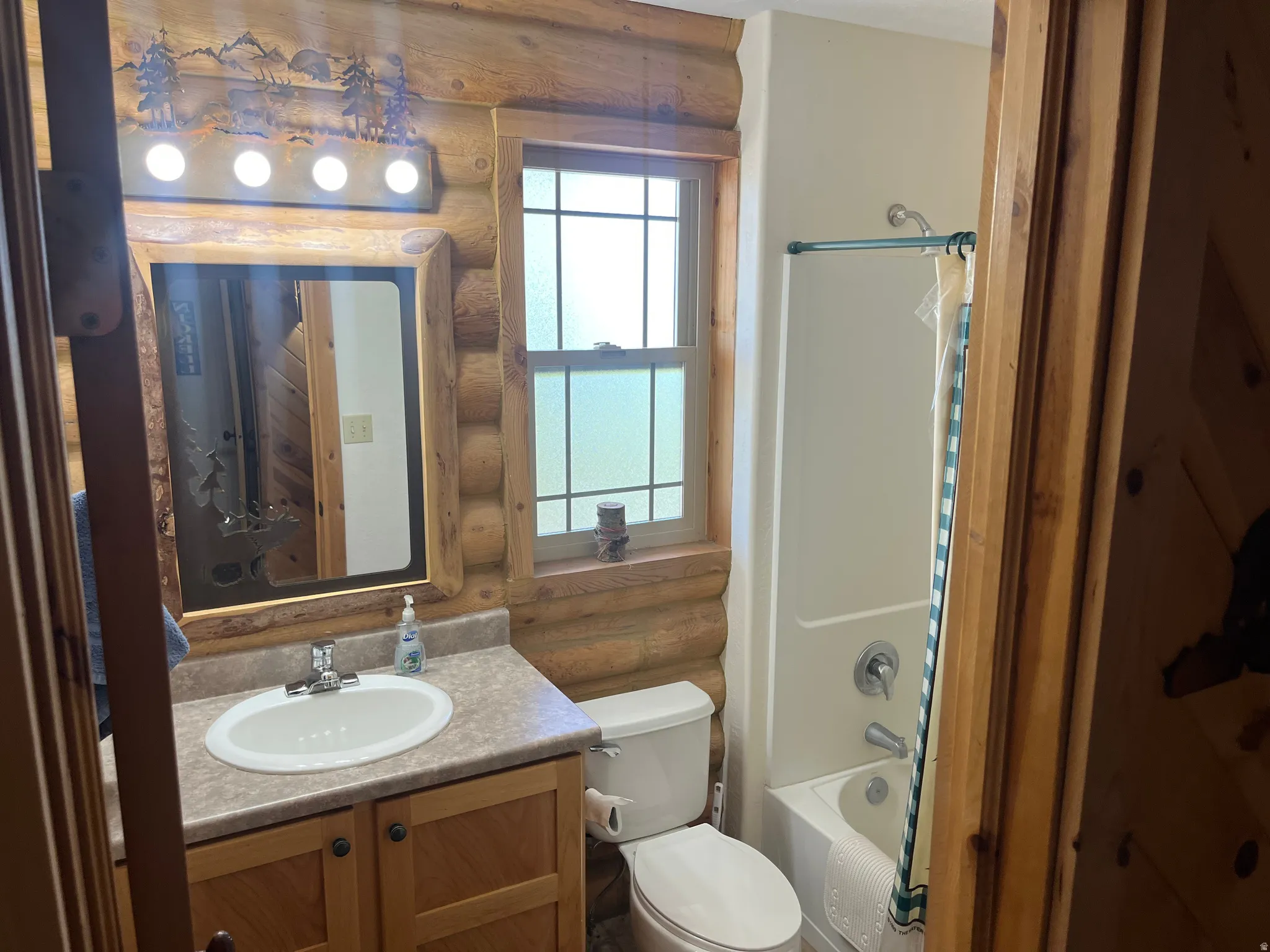 Bathroom featuring log-style walls, a vanity with a laminate countertop, a single basin sink, and wood cabinetry