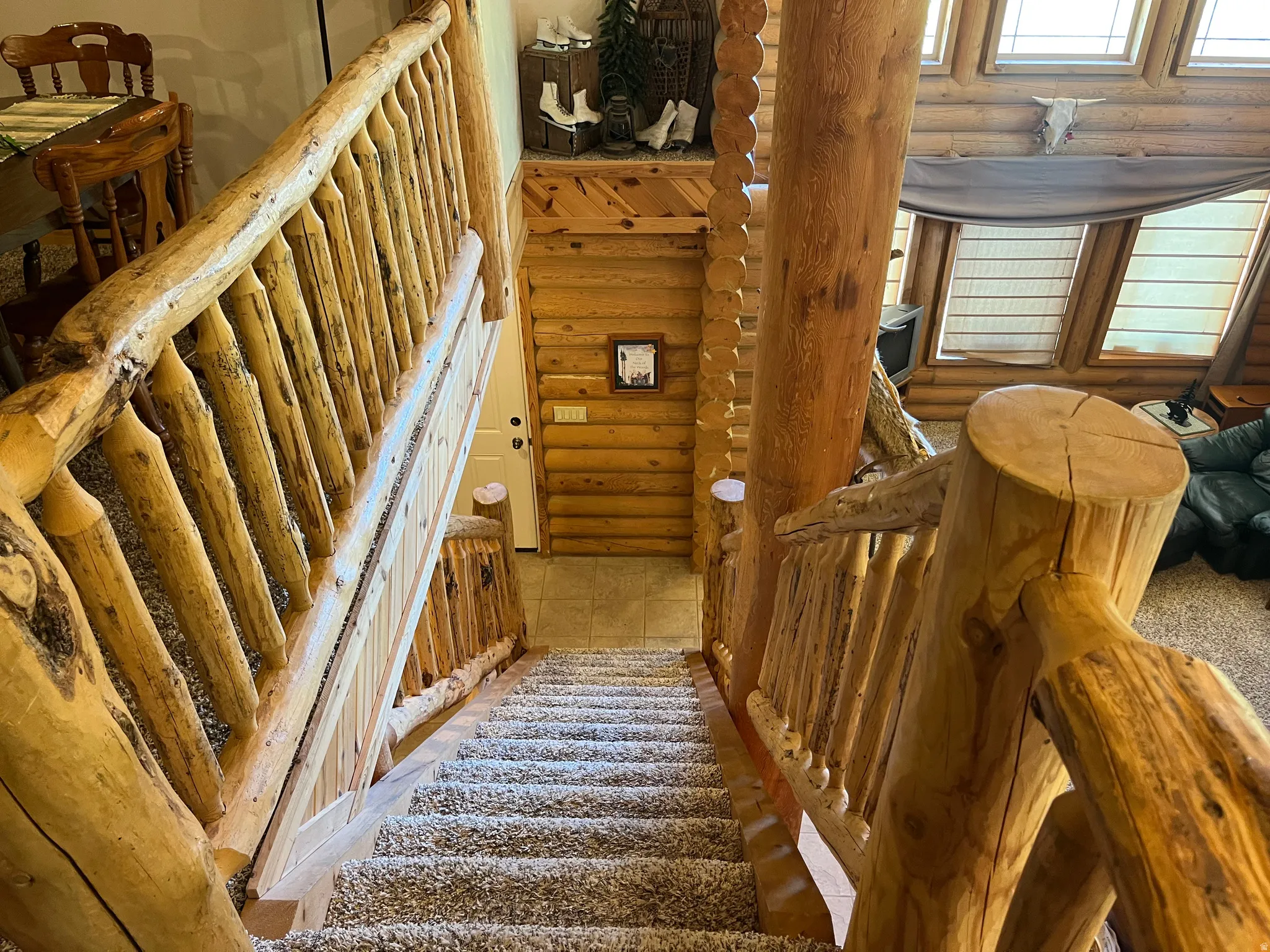 Log staircase with wood-finish railing, carpeted treads, and exposed log wall construction
