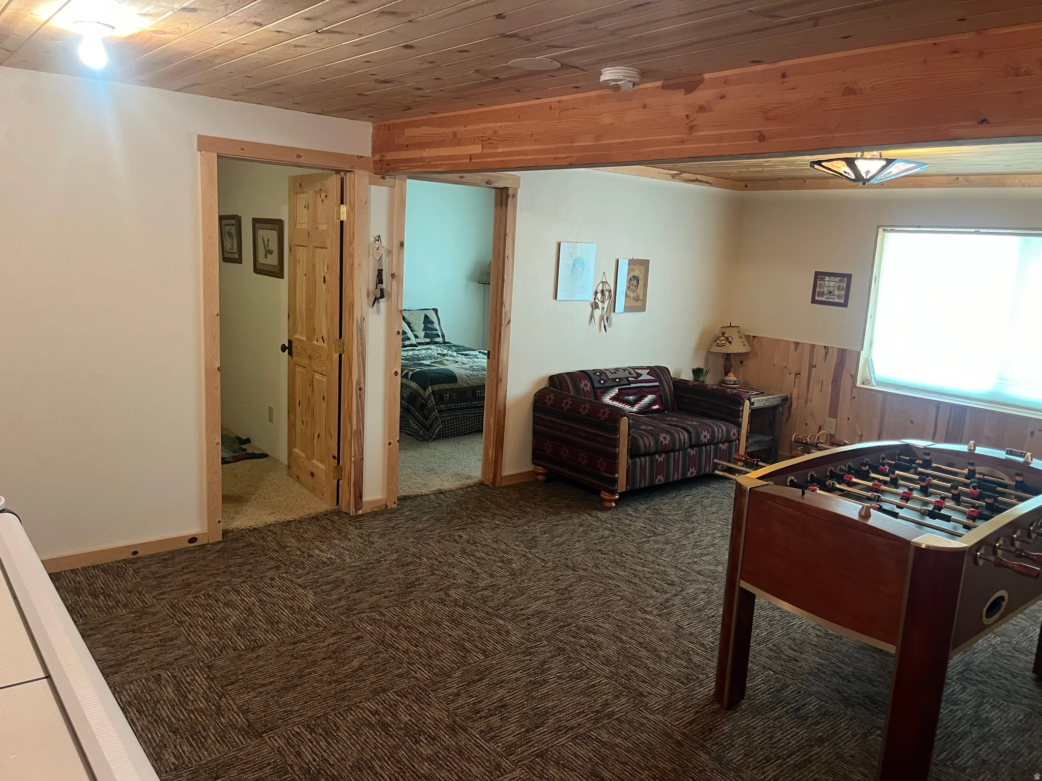 Carpet tile flooring throughout this recreation space, featuring exposed wood ceiling beams and wood-paneled walls