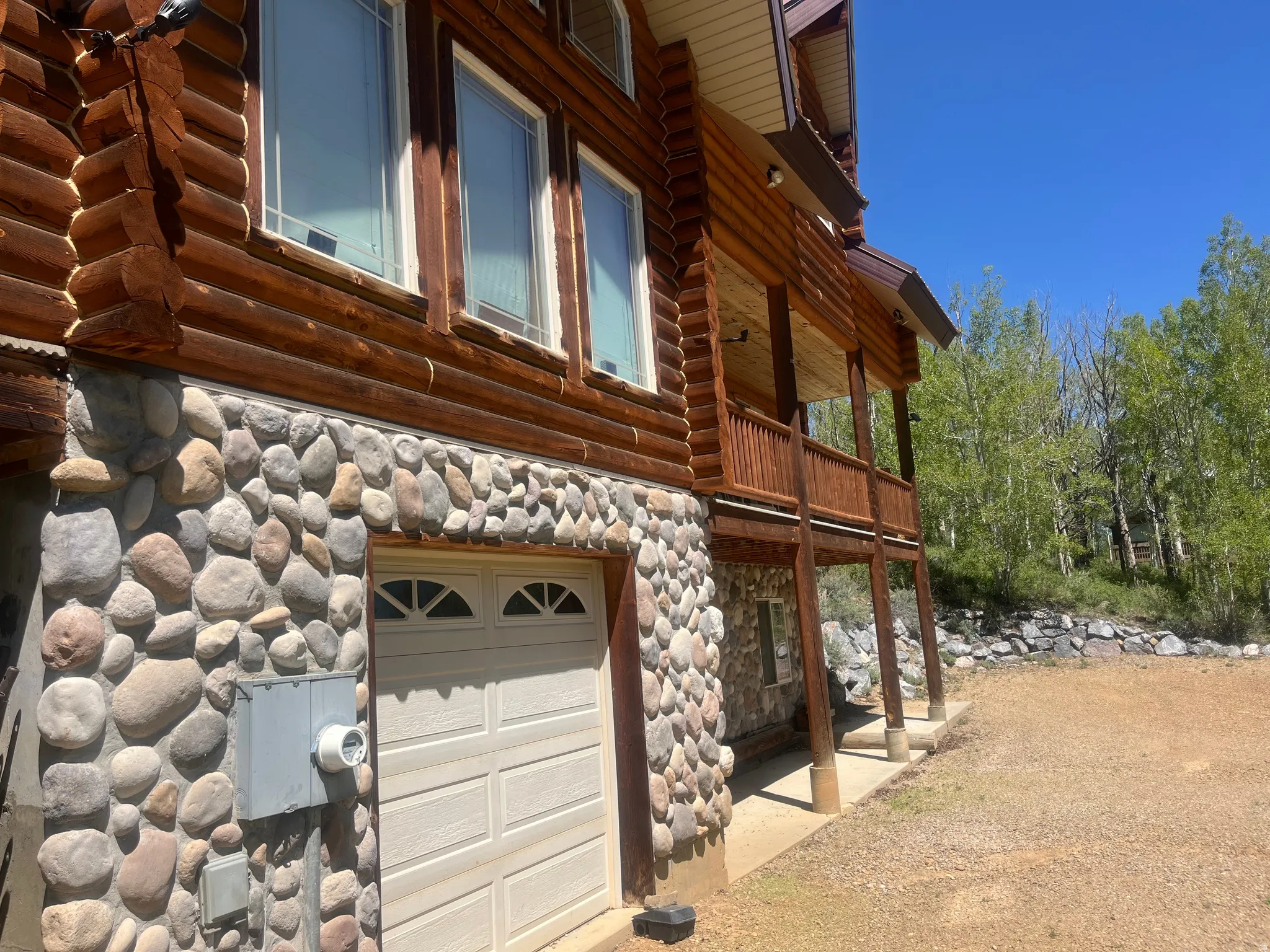 Log home exterior featuring a stone foundation, prominent wood log siding, and an upper-level balcony with wood railing