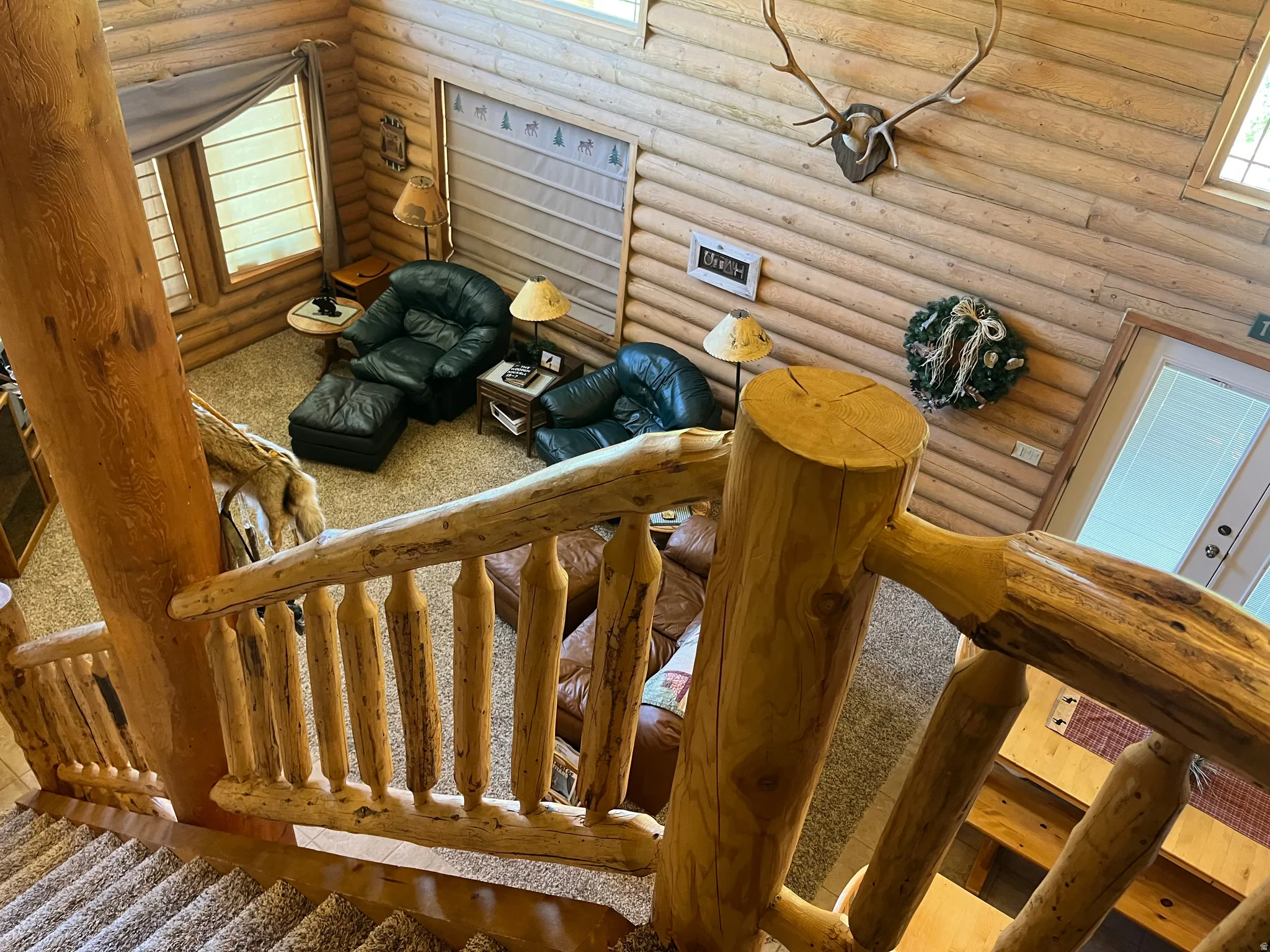 Rustic log-style interior featuring a log staircase and railing, textured wall paneling, and a carpeted floor