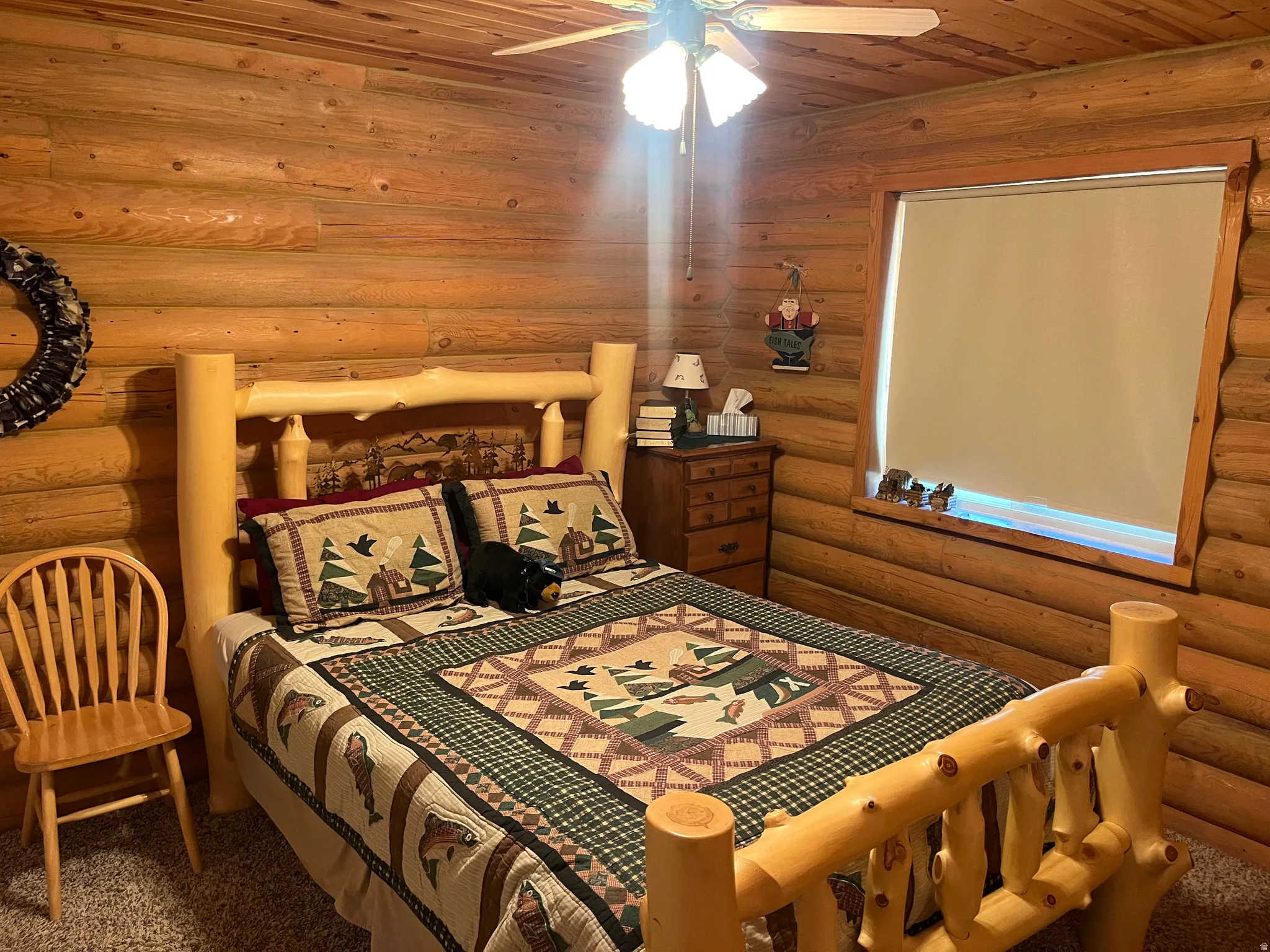 Log cabin interior featuring wood log walls, wood-finish ceiling, a window with wood trim, and a ceiling fan with integrated lighting