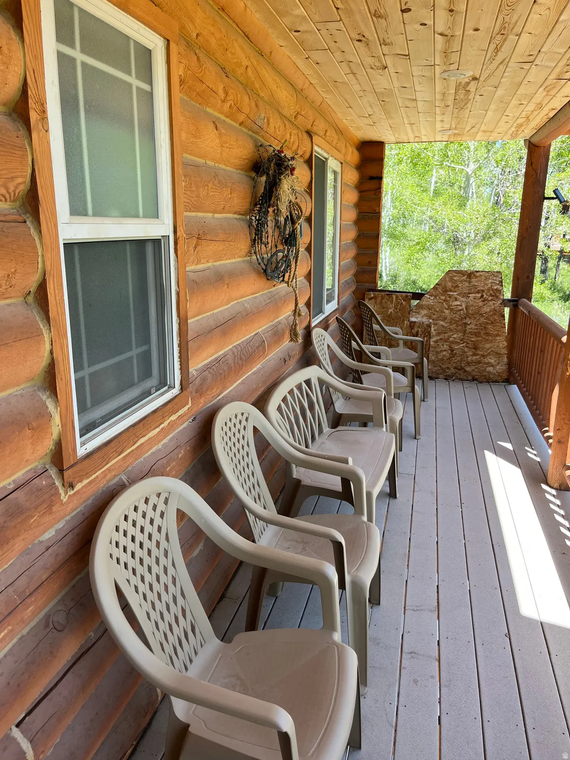 Covered porch featuring a log cabin exterior, wood plank ceiling, multiple windows, and a wood-finish floor