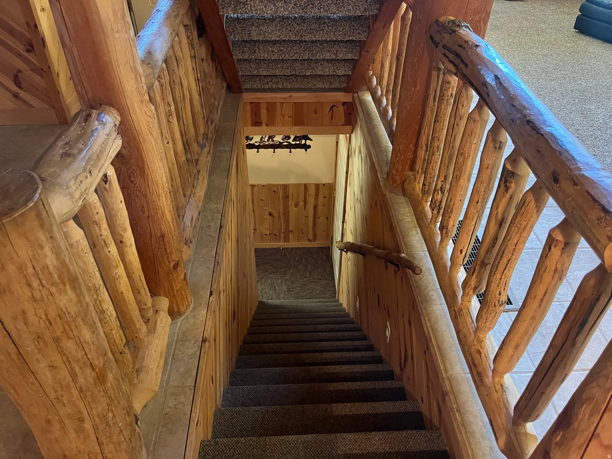 Carpeted staircase featuring natural wood log railings and wood-paneled walls