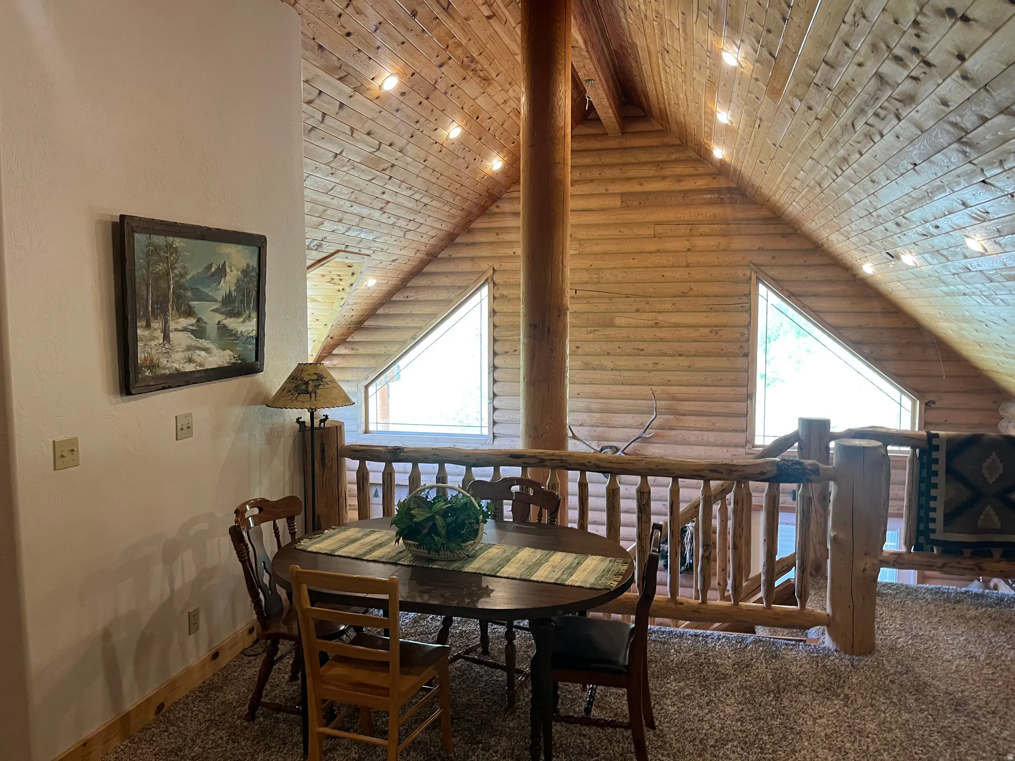 Vaulted wood-paneled ceiling with exposed wood beam, triangular windows, wood railing, and carpeted flooring