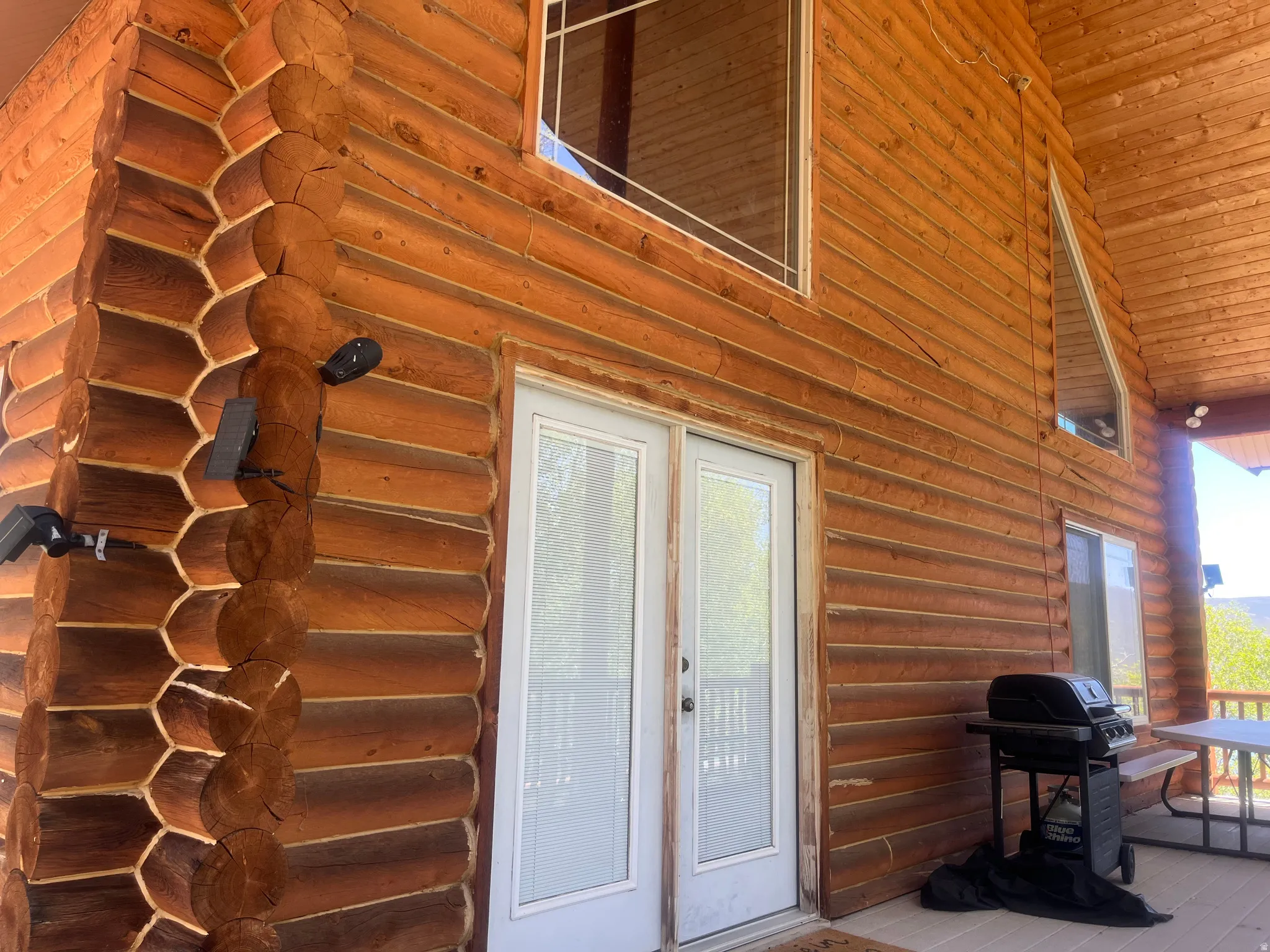 Log cabin exterior featuring a covered porch, white-framed glass paneled double doors, and additional windows