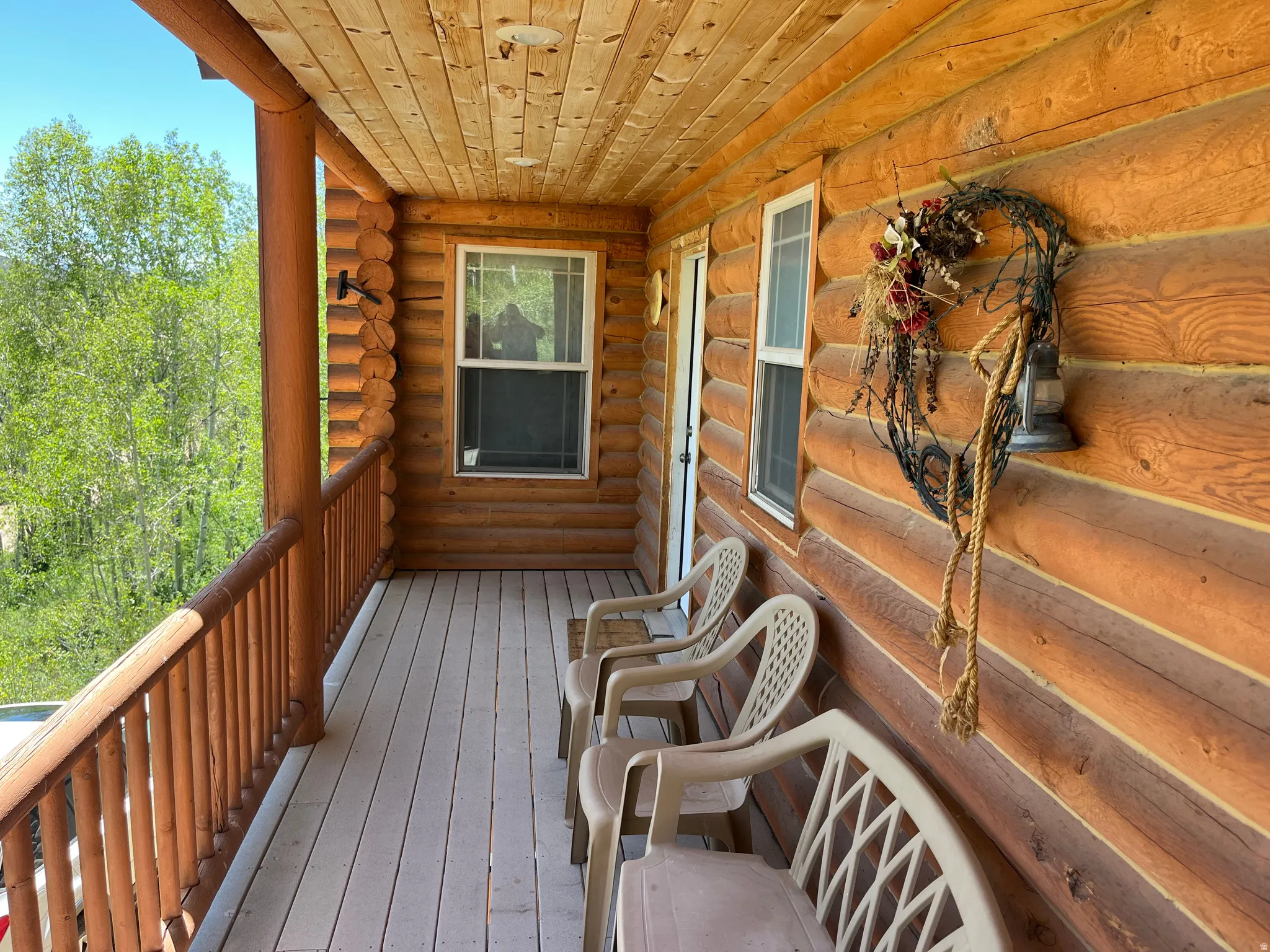 Covered log cabin porch with wood-finish ceiling, log railings, and light-colored composite decking