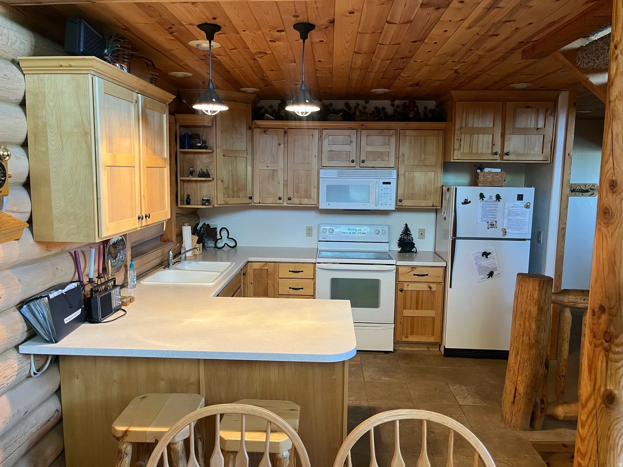 Kitchen featuring wood-paneled ceilings, white built-in appliances, light wood cabinetry, a double basin sink, and tile flooring