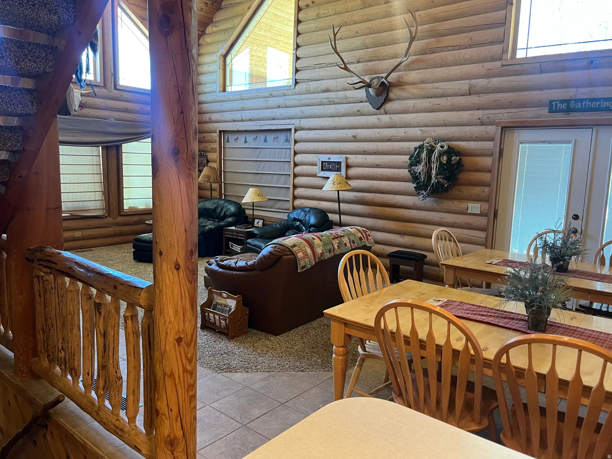 Open-concept living space featuring natural log walls and ceiling beams, large windows, and a carpeted floor