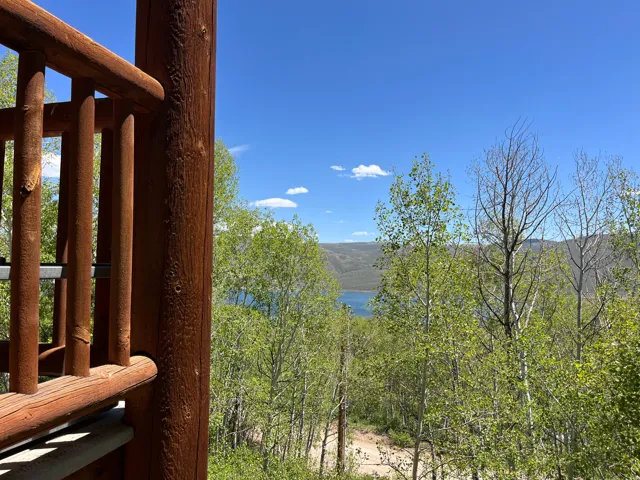 Wooden deck railing overlooking a treed landscape with water and mountains in the distance under a clear sky