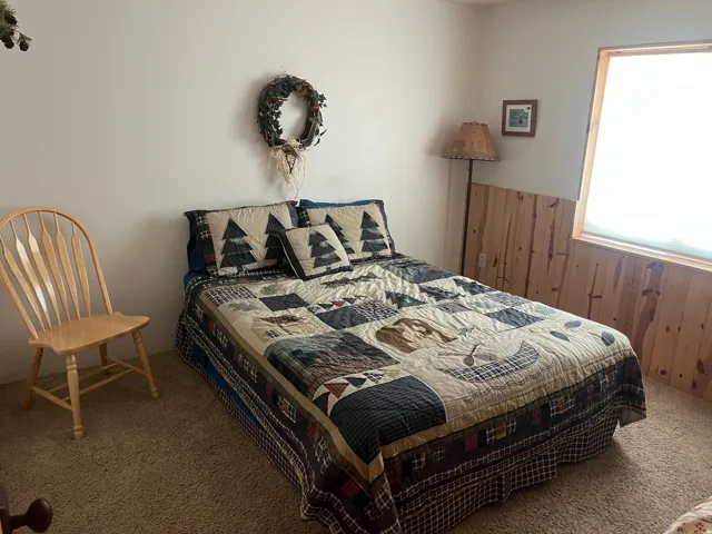 Bedroom featuring carpet flooring, natural wood paneling, and a wood-framed window