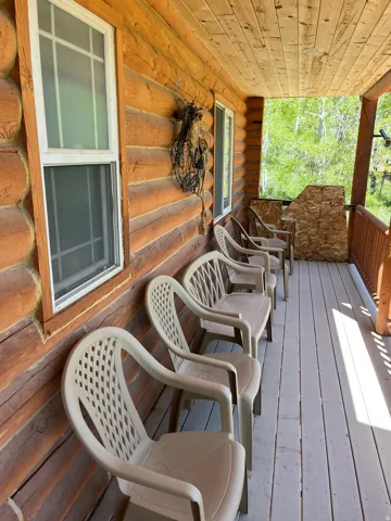 Covered porch featuring a log cabin exterior, wood plank ceiling, multiple windows, and a wood-finish floor