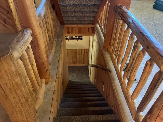 Carpeted staircase featuring natural wood log railings and wood-paneled walls