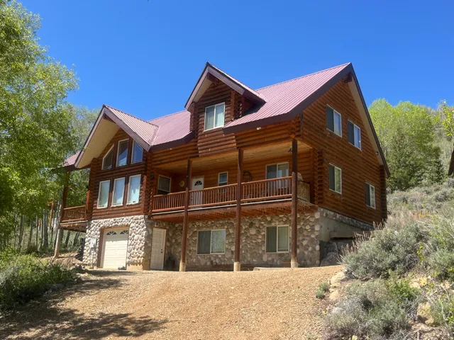 Log cabin exterior featuring a stone foundation, prominent front-facing gables, a red metal roof, and a covered balcony