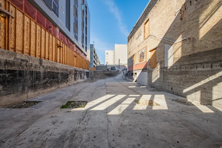 Concrete access path bordered by a multi-story structure with modern facade elements and a traditional brick building