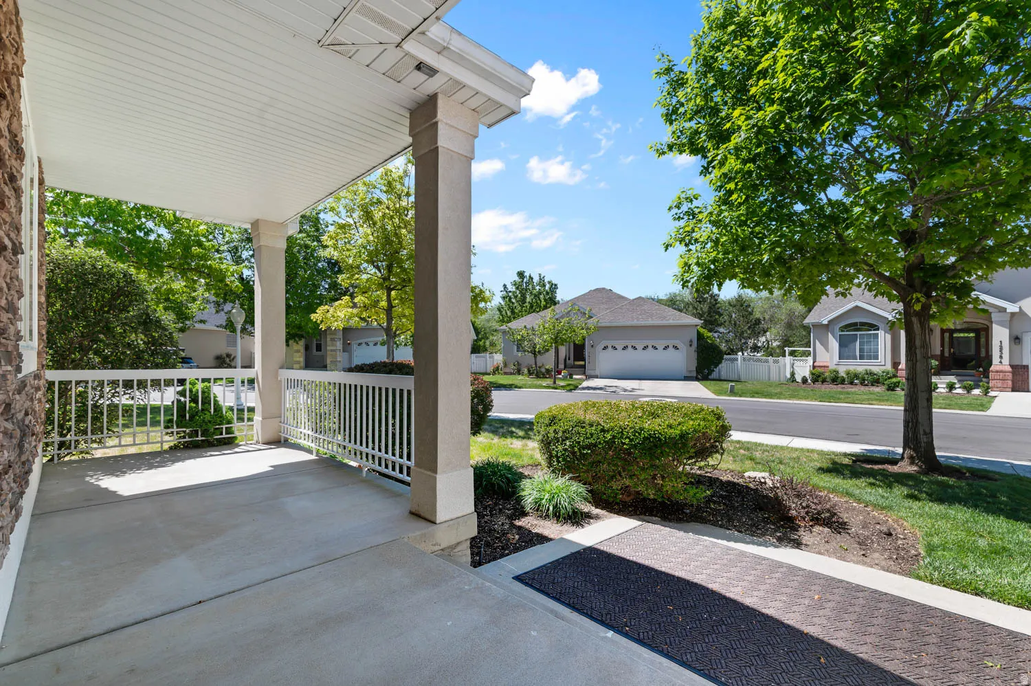 Covered concrete porch with white railing, stone facade, and mature landscaping