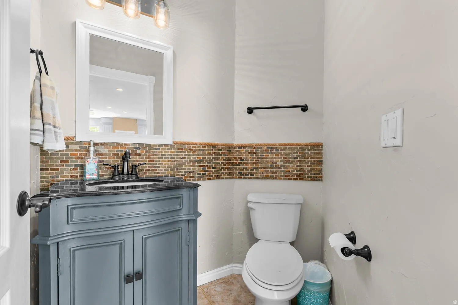 Bathroom featuring a gray vanity with a built-in sink, dark countertop, and mosaic tile backsplash
