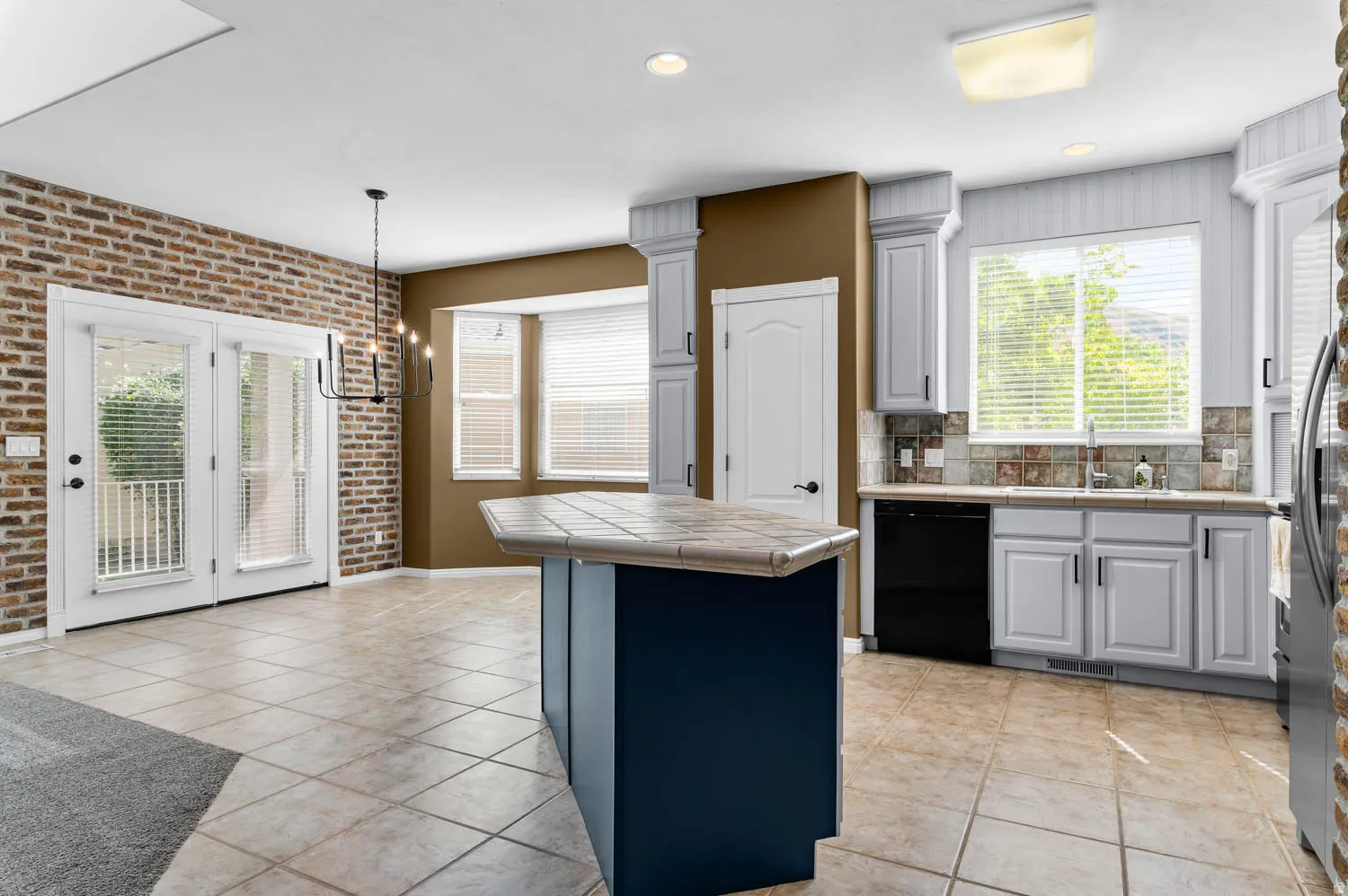 Kitchen featuring an island with a tiled countertop, light cabinetry, and black appliances