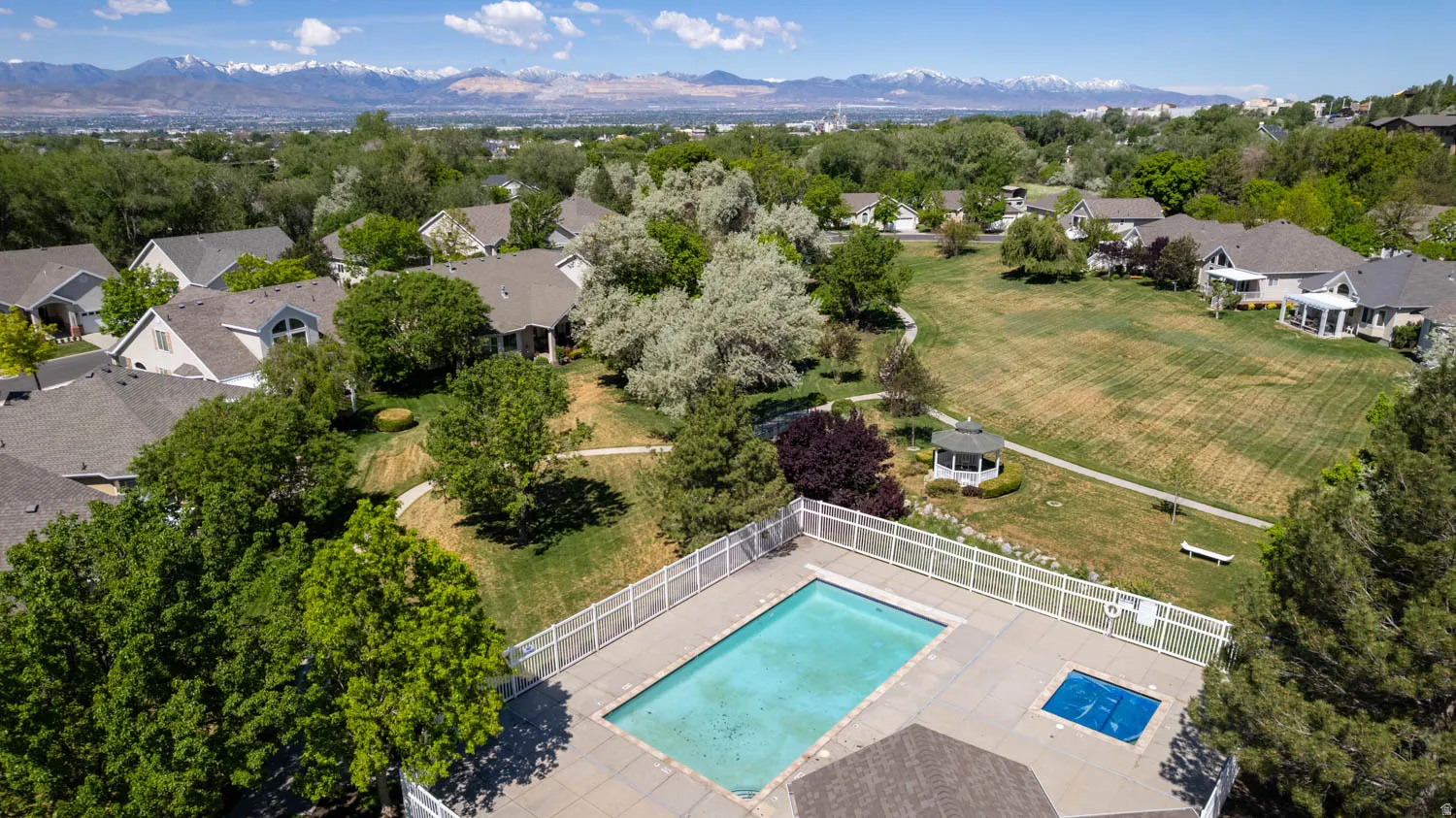 Community swimming pool with an integrated spa, surrounded by a white fence and extensive green spaces