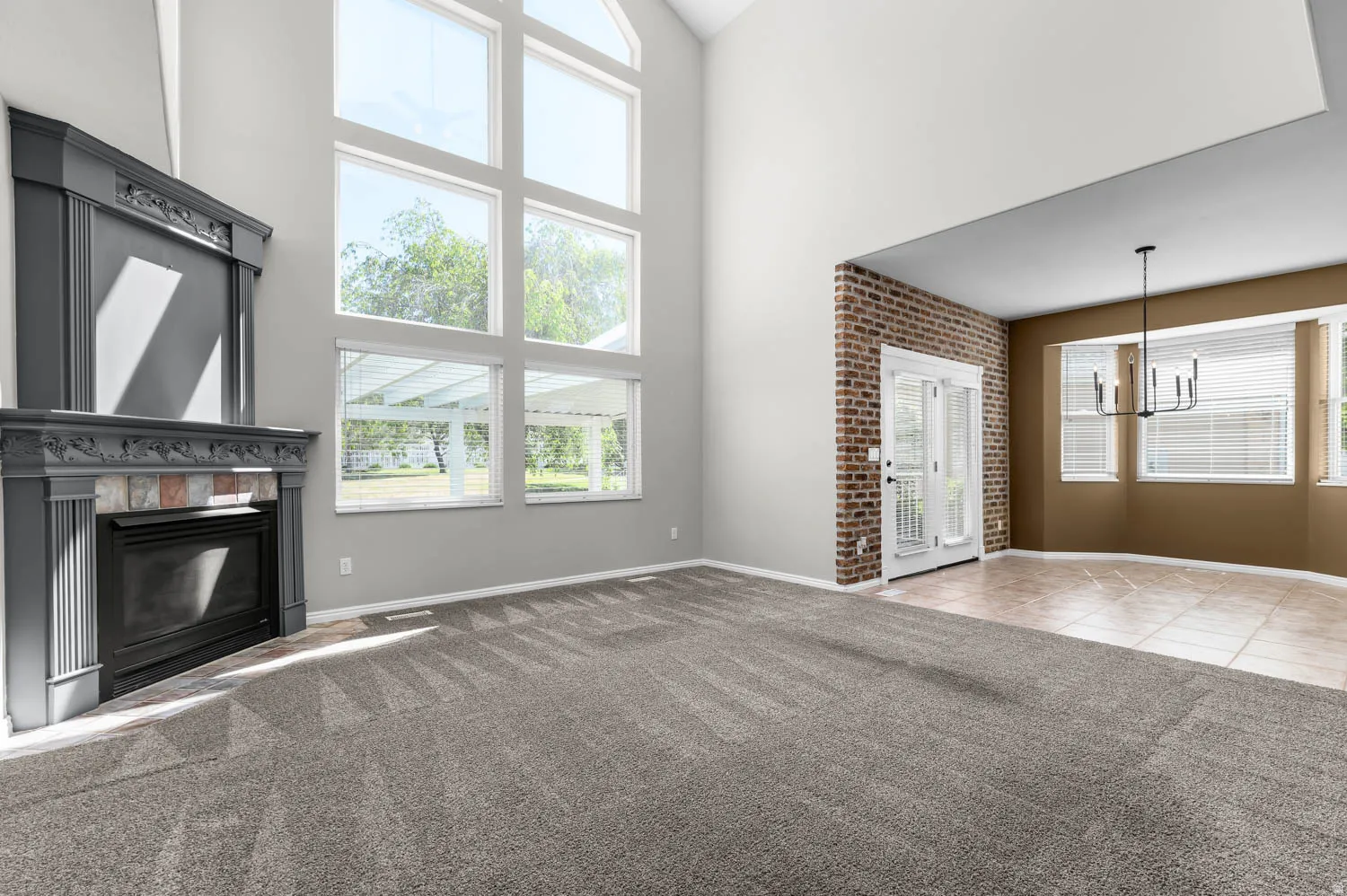 Vaulted ceiling living area featuring a fireplace with decorative mantel, expansive picture windows, and gray patterned carpeting
