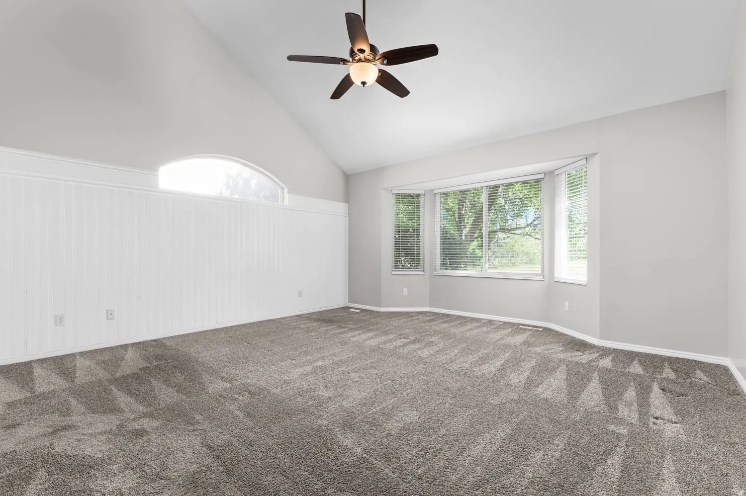 Spacious room with a vaulted ceiling, a multi-panel bay window, a semi-circular transom window, and white wainscoting